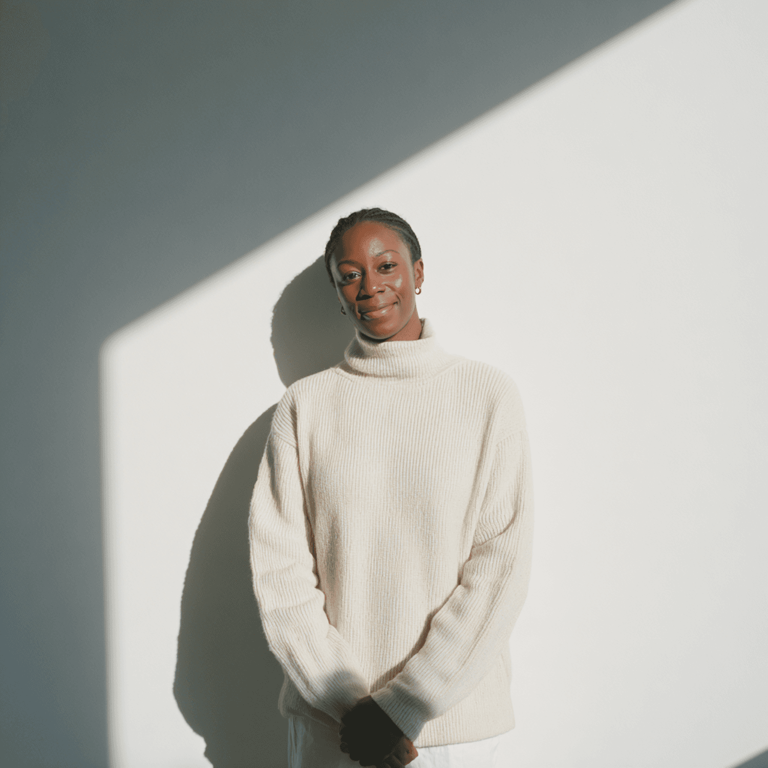Smiling woman with neat cornrows in a cream sweater, standing in warm sunlight